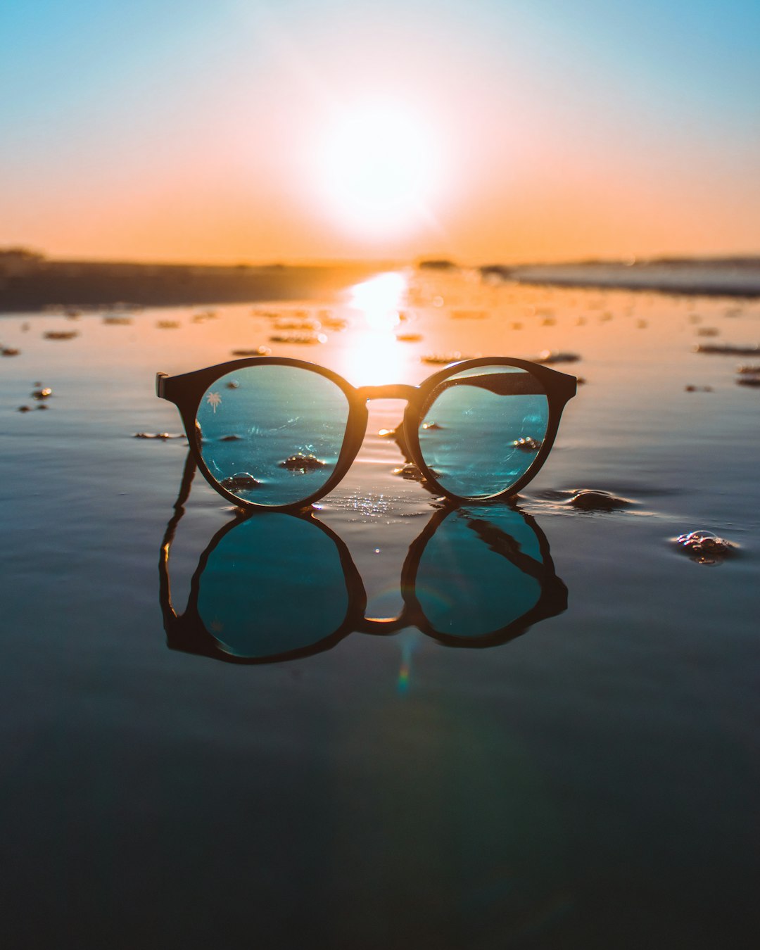 Sunglasses on the beach during a sunrise.