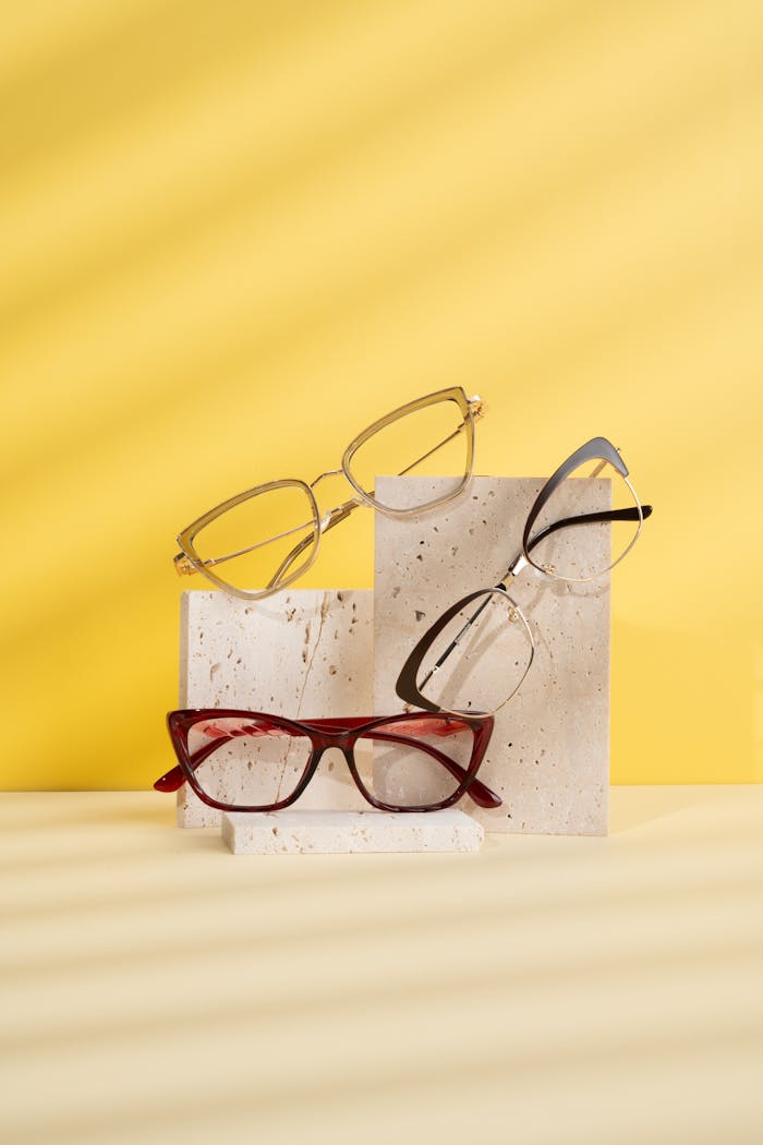 Stylish eyeglass frames showcased on textured blocks with a vibrant yellow backdrop.